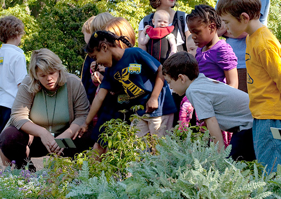 Instructor with young students crouched around plants
