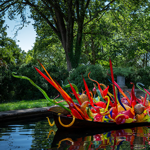 Boat full of multicolored glass spheres and tendrils floating in front of lush greenery