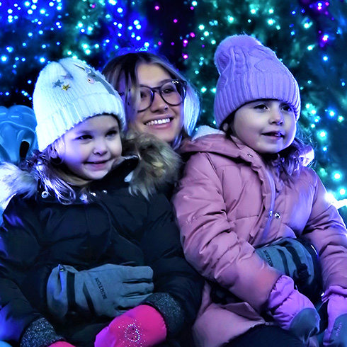 Adult with two children posing for photo surrounded by blue and purple lights