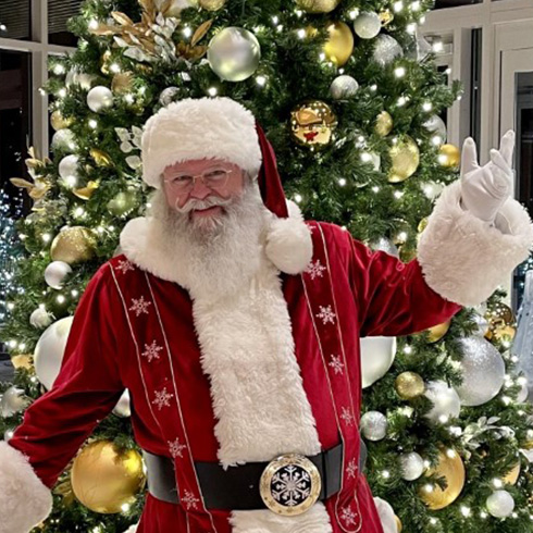 Santa Claus posing in front of tree decorated with white and gold ornaments