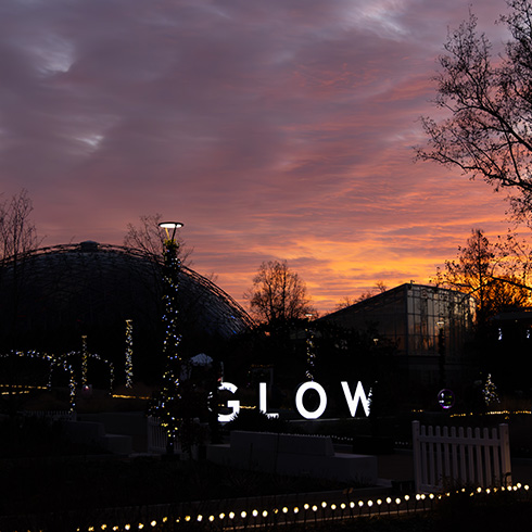 Illuminated GLOW letters under a sunset
