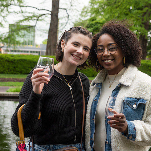 Visitors pose with wine glasses with glass atrium in background