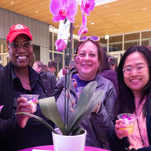 Group of friends enjoying drinks around blooming orchid under dramatic pink lighting