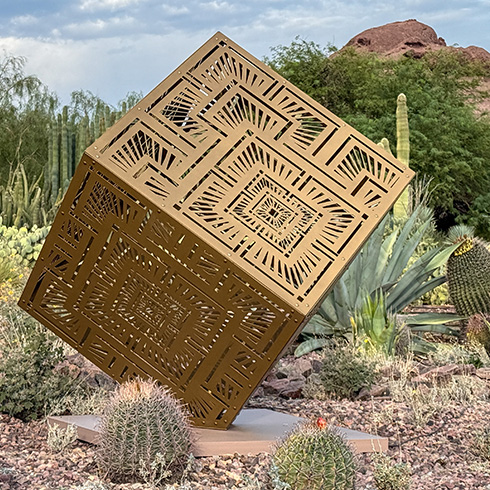 Large geometric sculpture reflecting sunlight in garden setting