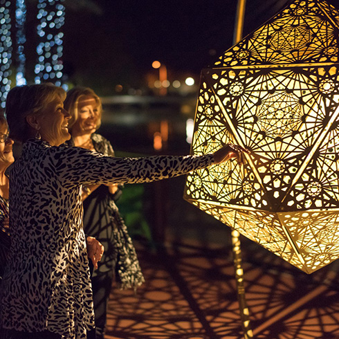 Adult touching large geometric sculpture lit from within at night