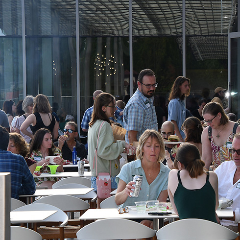 visitors dining and drinking on outdoor terrace with large glass windows in the background