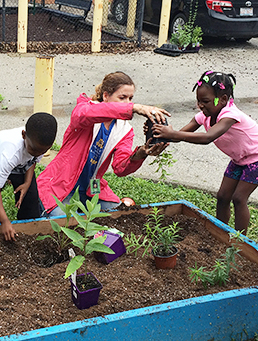 Teacher helping young children plant a schoolyard garden